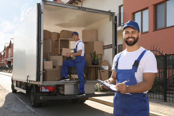 Moving service workers outdoors, unloading boxes and checking list - Фото, изображение