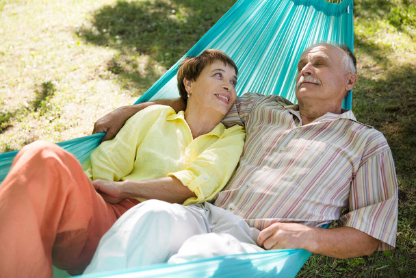 Happy senior couple rest in a hammock in a summer park or garden. Concept of friendly family. - Fotoğraf, Görsel