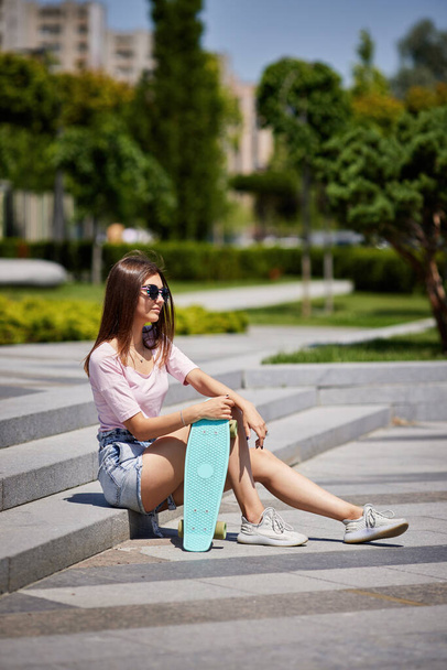 beautiful skateboarder girl with skateboard sitting outdoors - Фото, зображення
