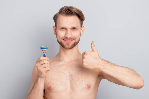 Photo of nice young blond man hold razor show thumb up without clothes isolated on grey color background - Foto, afbeelding