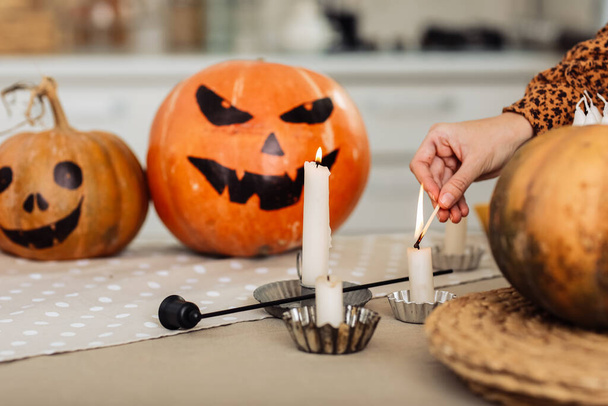 Ferien- und Freizeitkonzept - Frauenhand mit Streichhölzern, die zu Hause zu Halloween Kerzen anzünden. bemalte Kürbisse auf einem Hintergrund. Horror-Thema und Hallowe 'en. Selektiver Fokus - Foto, Bild