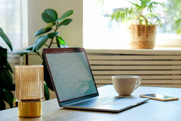 Home office concept. Designated work from home area near the window. Modern laptop, notebook and vase with flowers on table. Close up, copy space, background. - Foto, afbeelding