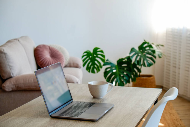 Home office concept. Designated work from home area near the window. Modern laptop, notebook and vase with flowers on table. Close up, copy space, background. - Fotoğraf, Görsel