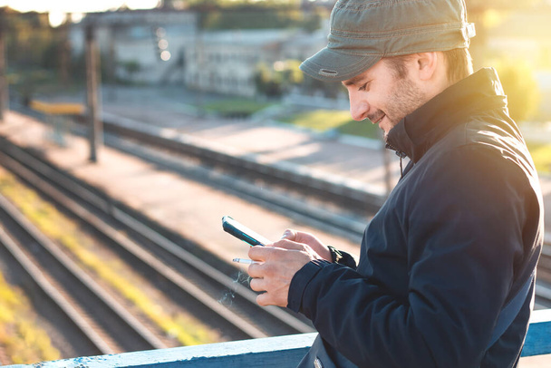 Un hombre con teléfono en la estación de tren. Joven hombre feliz usando smartphone en la ciudad - Foto, imagen