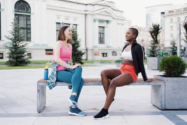 Egzersiz sonrası rahatlayan iki farklı ırktan kıvrımlı kız, açık havada iletişim kuruyor.. - Fotoğraf, Görsel