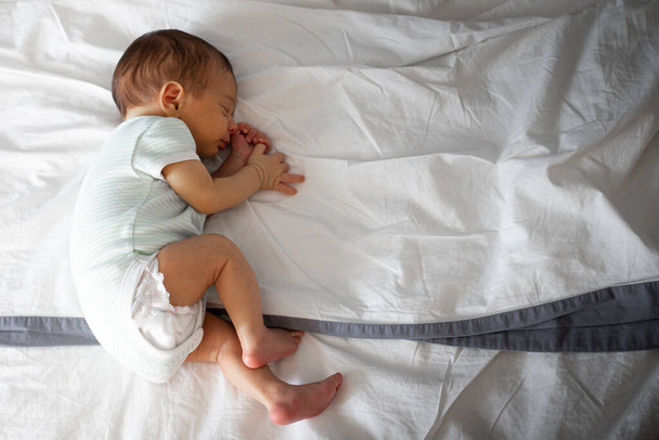 2 Monate altes kaukasisches Neugeborenes, allein im Bett der Eltern schlafend, auf der Seite liegend. Hintergrund mit Kopierraum. - Foto, Bild