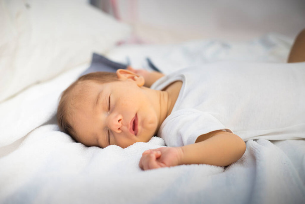 Белый новорожденный спит, лежит на спине, на белом и сером постельном белье. Принято. Вид сбоку. - Фото, изображение