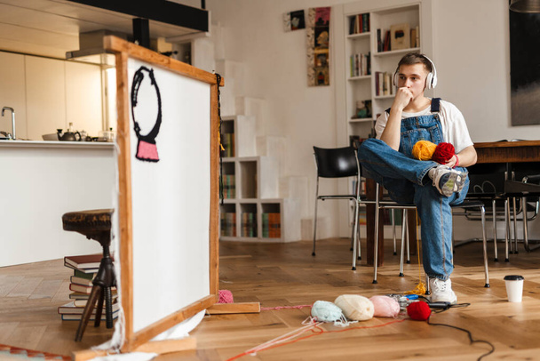 Young white man in headphones working on craft rug at home - Foto, Bild