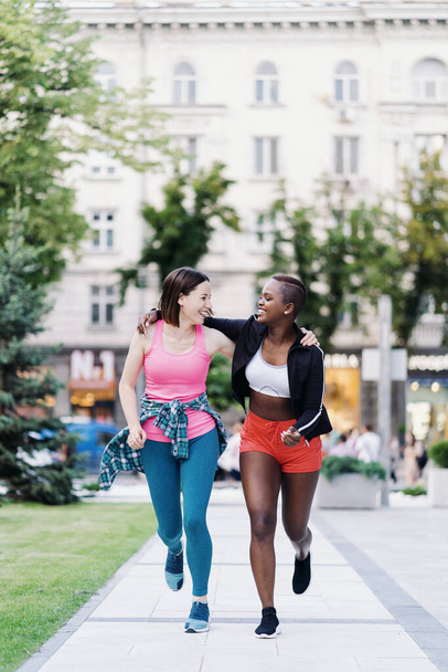 Due ragazze multietniche che corrono per le strade della città, comunicando all'aperto. - Foto, immagini