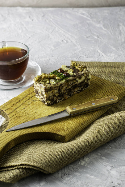 um pedaço de gergelim caseiro tahini halva em uma tábua de madeira perto - ao lado de uma faca e uma xícara de chá. Foto de alta qualidade - Foto, Imagem
