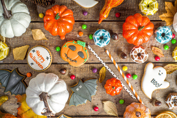 Halloween cookies, sweets and decor background. Trick or treat concept. Traditional halloween gingerbread, candy with pumpkins and decorations on wooden background top view copy space - Foto, Bild