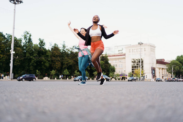 Two multiethnic girls running through the city streets, outdoor communicating. - Fotó, kép