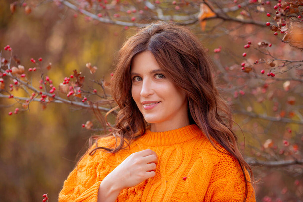 Sonbahar parkında turuncu kazaklı genç bir kadın. - Fotoğraf, Görsel