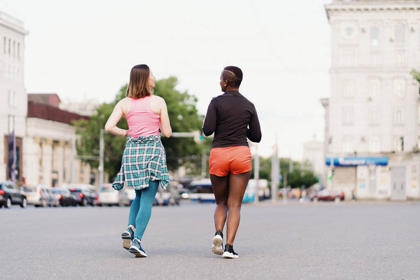 Twee multi-etnische meisjes rennen door de straten van de stad, buiten communiceren. - Foto, afbeelding