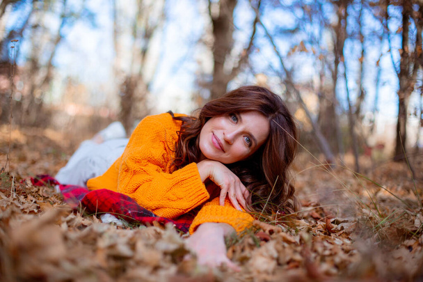 μια νεαρή γυναίκα σε ένα πάρκο του φθινοπώρου σε ένα πορτοκαλί πουλόβερ - Φωτογραφία, εικόνα