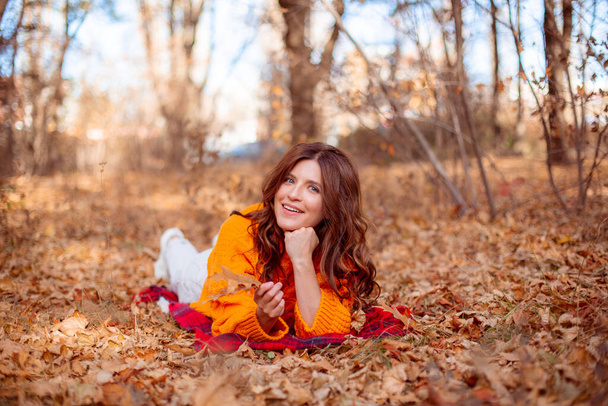een jonge vrouw in een herfstpark in een oranje trui - Foto, afbeelding