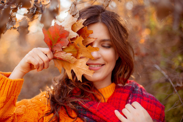 オレンジ色のセーターを着た秋の公園の若い女性が - 写真・画像