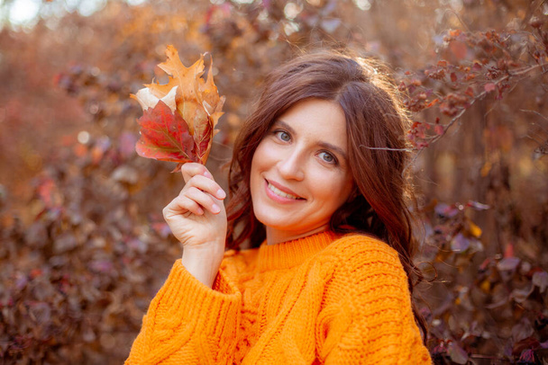 молодая женщина в осеннем парке в оранжевом свитере - Фото, изображение
