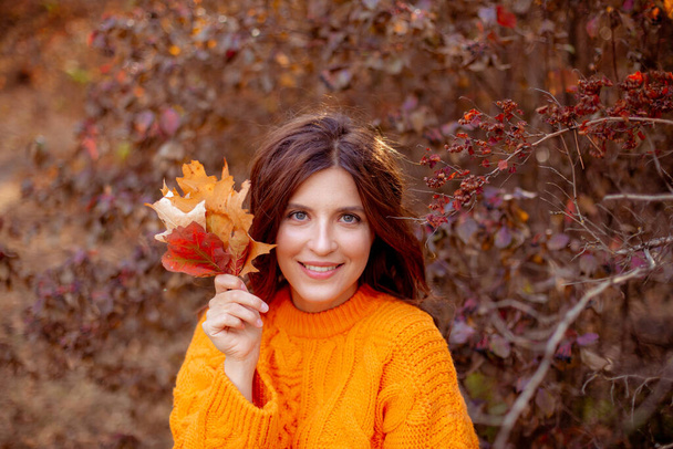 молодая женщина в осеннем парке в оранжевом свитере - Фото, изображение