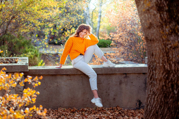 a young woman in an autumn park in an orange sweater - Photo, Image