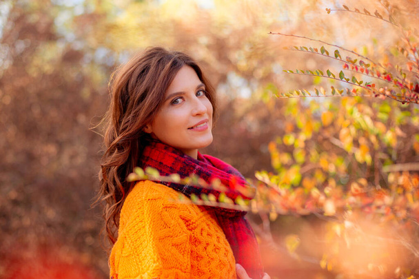 молодая женщина в оранжевом свитере завернулась в шарф в осеннем парке - Фото, изображение
