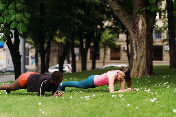 Twee mooie vrouwen maken plank op het stadsplein tijdens sportactiviteiten - Foto, afbeelding