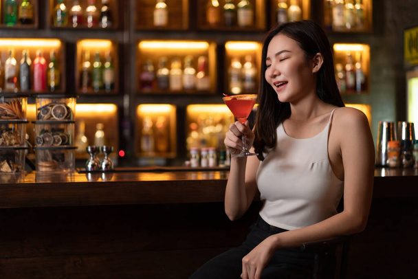 Nightlife-Konzept: Eine junge Frau in sexy Outfits hält ein Glas rosa Flüssigkeit in der Hand und genießt seinen Geschmack im schummrigen Licht der Bar. - Foto, Bild