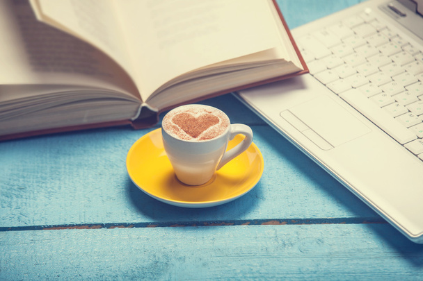 Tasse Kaffee mit Laptop und Buch auf blau Holztisch. - Foto, afbeelding