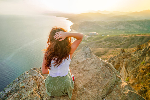 Panoramafoto einer glücklichen Frau mit offenen Händen, die die Spitze einer Klippe mit einem schönen Blick auf das Meer und das Stadtbild eroberte. Das Konzept des Reisens und der Freiheit. - Foto, Bild