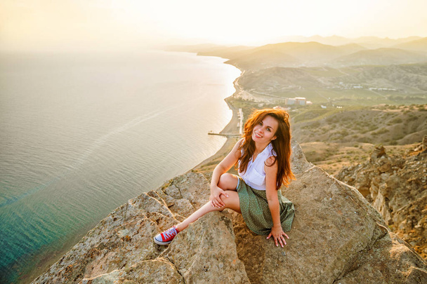 Panoramiczne zdjęcie szczęśliwej kobiety z otwartymi rękami, która podbiła szczyt klifu z pięknym widokiem na morze i krajobraz miasta. Pojęcie podróży i wolności. - Zdjęcie, obraz