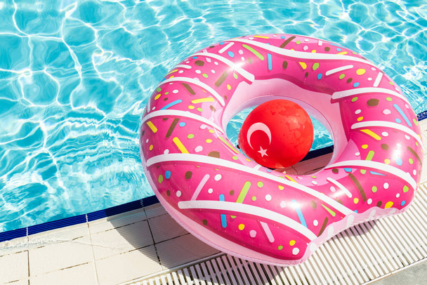 Inflatable children's playground in the form of a pink donut and a red ball in the form of the national flag of Turkey on the water in the poo - 写真・画像