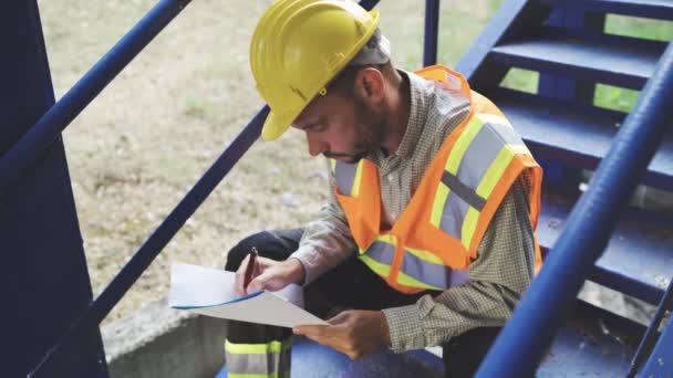 Architect in helmet and safety vest making notes in notepad - Footage, Video