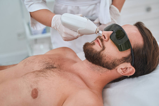 Νεαρός πελάτης spa με γυαλιά ασφαλείας κατά τη διάρκεια μιας αισθητικής διαδικασίας - Φωτογραφία, εικόνα
