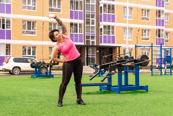young strong woman doing warm-up before workout on the sports ground with outdoor gym equipment in front of the house - Foto, imagen