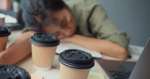 Szabadúszó Ázsia kimerült hölgy kemény munka alszik sok papír csésze kávé fa asztal az irodában. Otthoni nappaliból dolgozik, távolról, társadalmi távolságtartás, karantén a koronavírus számára. - Felvétel, videó