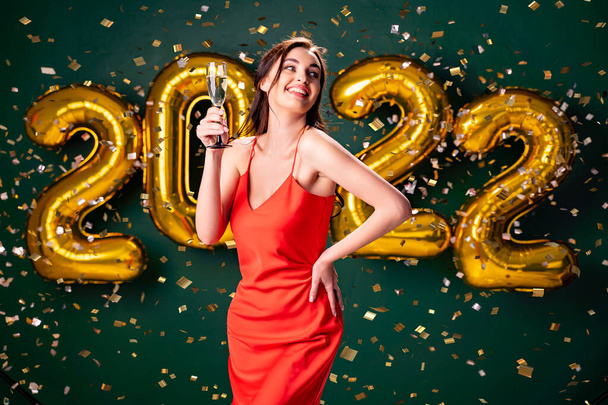 New Year party. 2022 air balloons confetti green background. Woman with champagne. Celebrate  - 写真・画像