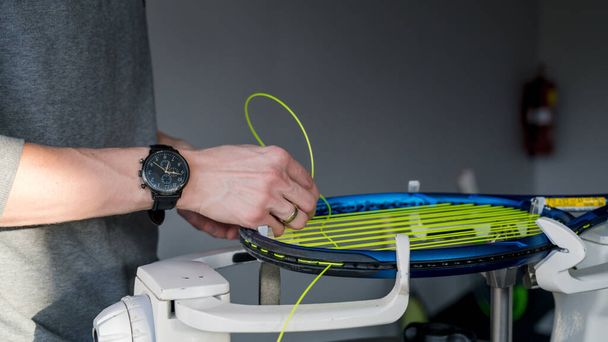Κοντινό πλάνο της ρακέτας του τένις στην ηλεκτρονική μηχανή. Διαδικασία αντικατάστασης συνθετικής χορδής εντέρου πριν από το παιχνίδι. Χέρια του σφιγκτήρα. - Φωτογραφία, εικόνα