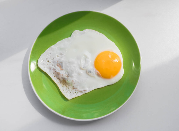A freshly cooked hot fried egg sits on a green plate. Healthy breakfast. Close-up. View from above. - Фото, зображення