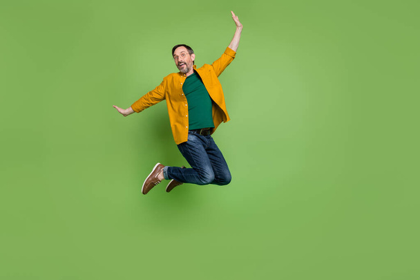 Volledige lengte foto van vrolijke vrolijke volwassen man springen op genieten weekend glimlach geïsoleerd op groene kleur achtergrond - Foto, afbeelding