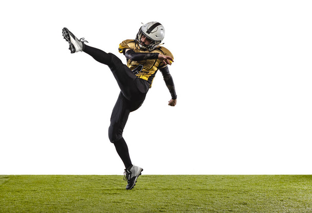 One professional american football player in special uniform kicking ball with leg isolated over white grass flooring background - Foto, immagini