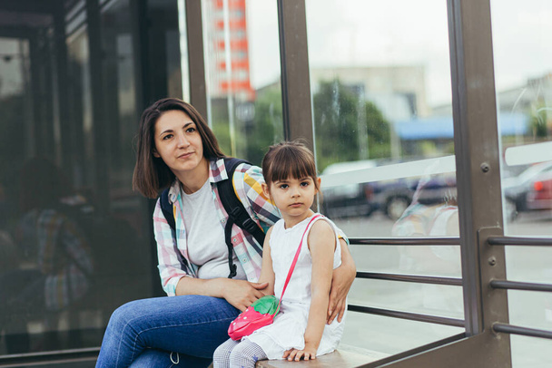 Młoda kobieta z córką czeka na publiczny autobus na dworcu autobusowym. - Zdjęcie, obraz