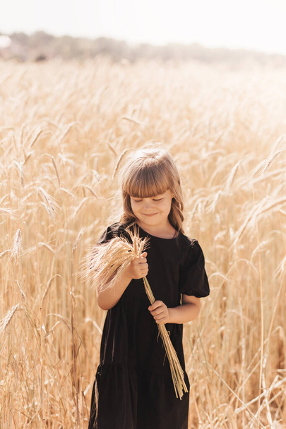 A little cute girl with long hair holds spikelets of wheat in the field in the summer. Summer. Harvest concept - Fotoğraf, Görsel
