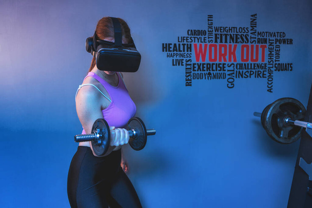Attractive young red hair sportswoman training biceps in the gym of her beautiful house with vr futuristic goggles - Ginger athletic model doing home sport pilates workout exercises during quarantine - Photo, Image