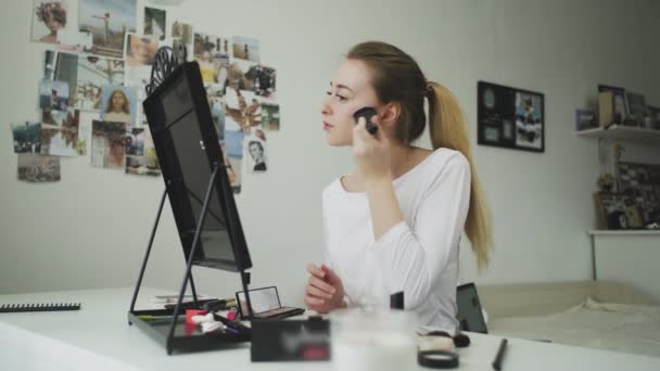 Μια νεαρή γυναίκα κάνει το μακιγιάζ της, ενώ κάθεται σε ένα τραπέζι μπροστά από έναν καθρέφτη - Πλάνα, βίντεο