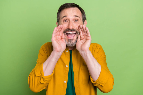 Photo of cheerful positive mature man hold hands face mouth tell information isolated on green color background - 写真・画像