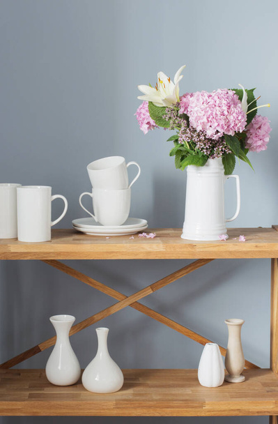 white cups and flowers on vase  on wooden shelf on gray background - Foto, imagen
