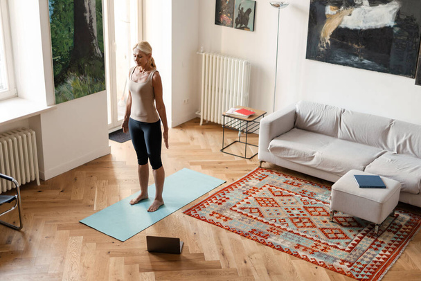 Blonde mature woman using laptop during yoga practice at home - Foto, Imagem