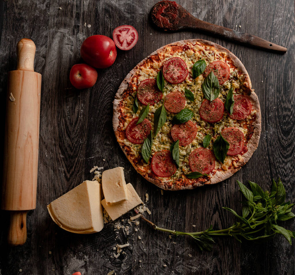 A top view of a gourmet pizza and ingredients on a wooden board - Foto, Imagem