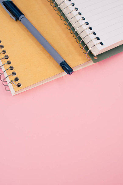 A vertical shot of an open notebook with a pen on a pink background with copy space - Fotografie, Obrázek