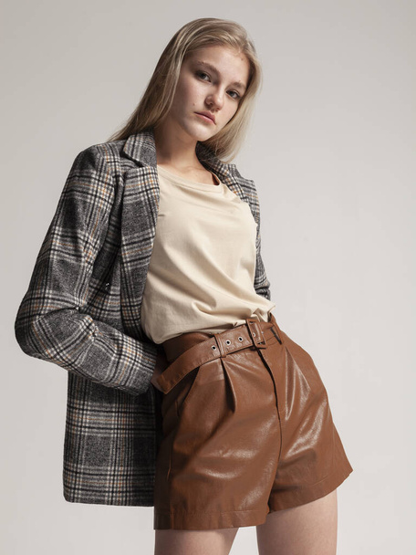 portrait of a blonde in a plaid jacket and leather shorts on a gray background - Fotoğraf, Görsel
